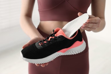 Photo of Sporty woman putting orthopedic insole into shoe on blurred background, closeup. Foot care