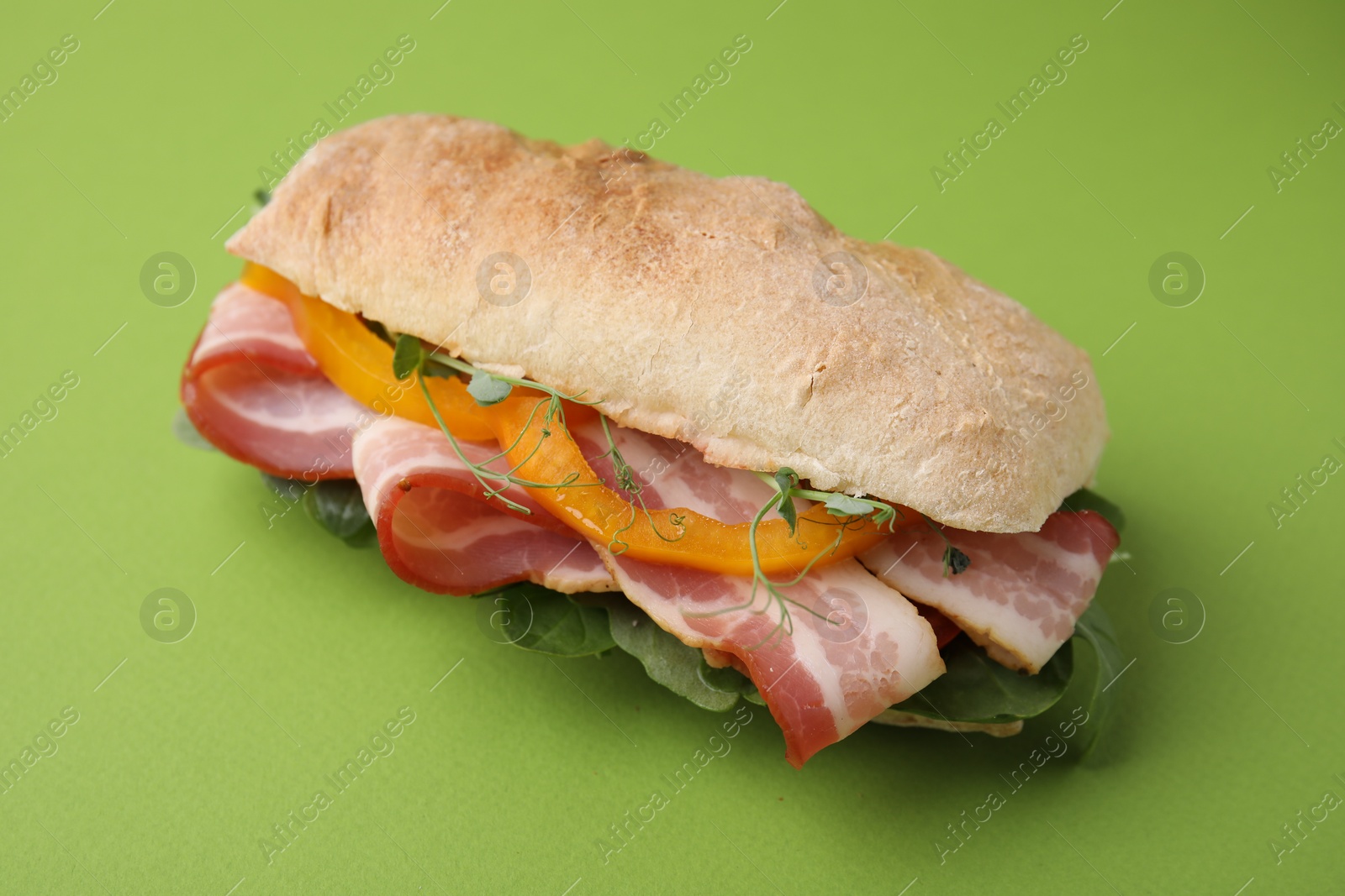 Photo of Tasty sandwich with bacon and bell pepper on green table