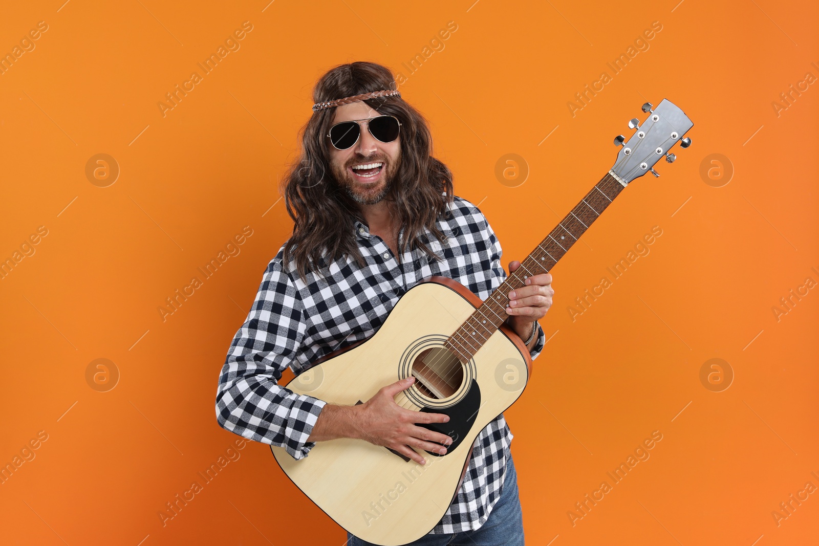Photo of Hippie man in sunglasses playing guitar on orange background