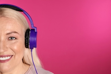 Photo of Mature woman enjoying music in headphones on color background, closeup. Space for text