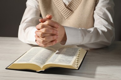 Woman praying over Bible at white wooden table, closeup