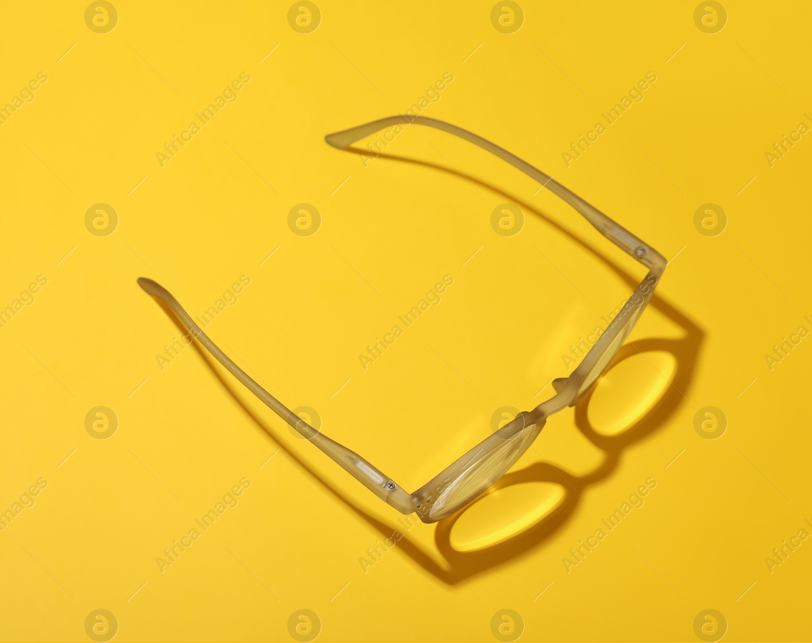 Photo of Glasses with corrective lenses on yellow background, above view