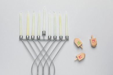 Hanukkah menorah with candles and dreidel on light background, flat lay