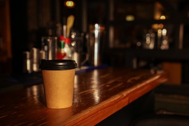 Photo of Paper coffee cup on wooden table in cafe. Space for text