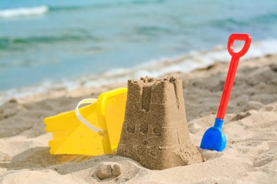 Photo of Beautiful sand castle, child plastic shovel and bucket on beach near sea