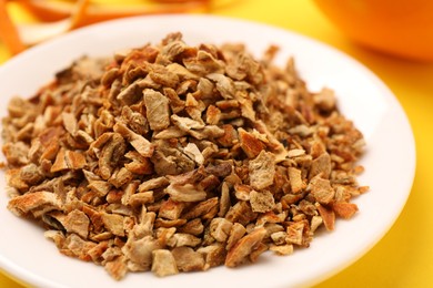 Plate with dried orange zest seasoning, fresh peel and fruit on yellow background, closeup