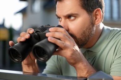 Concept of private life. Curious man with binoculars spying on neighbours over fence outdoors, closeup