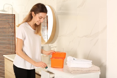 Photo of Woman putting laundry detergent capsule into washing machine indoors