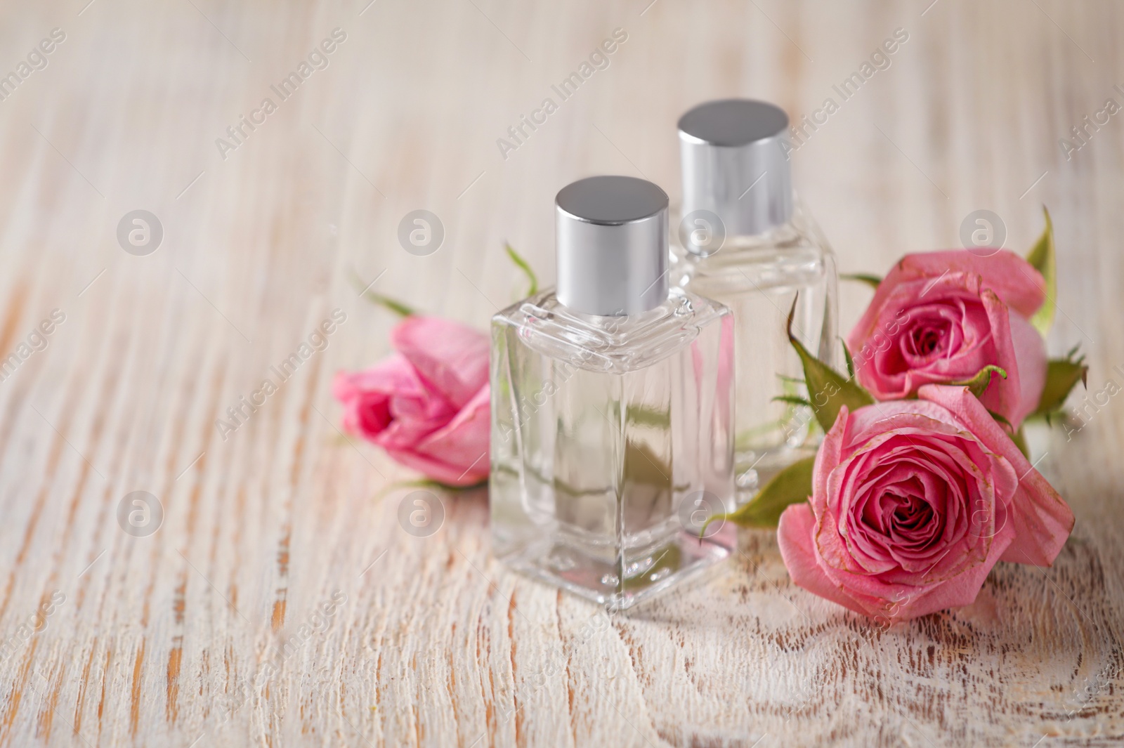 Photo of Bottles of essential oils and roses on white wooden table, space for text