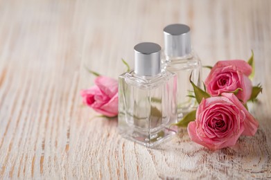 Bottles of essential oils and roses on white wooden table, space for text