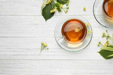 Cups of tea and linden blossom on white wooden table, flat lay. Space for text