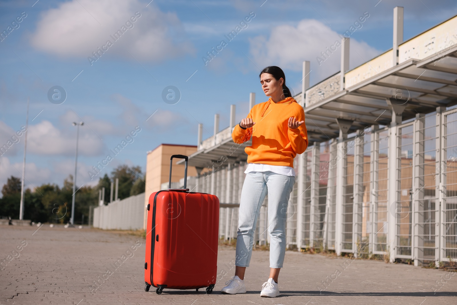 Photo of Being late. Worried young woman with red suitcase outdoors