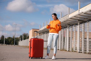 Photo of Being late. Worried young woman with red suitcase outdoors