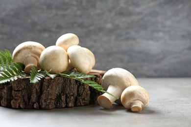Photo of Fresh champignon mushrooms with wooden stump and leaf on table