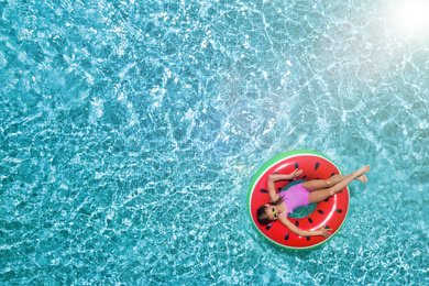 Cute little girl with inflatable ring in swimming pool, top view. Space for text 