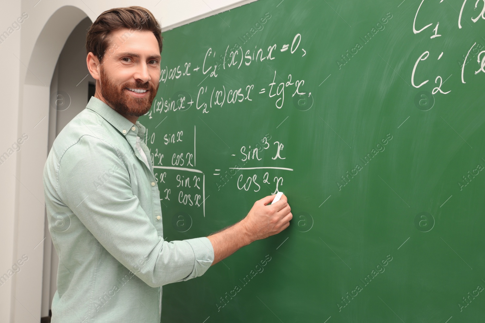 Photo of Happy teacher explaining mathematics at chalkboard in classroom