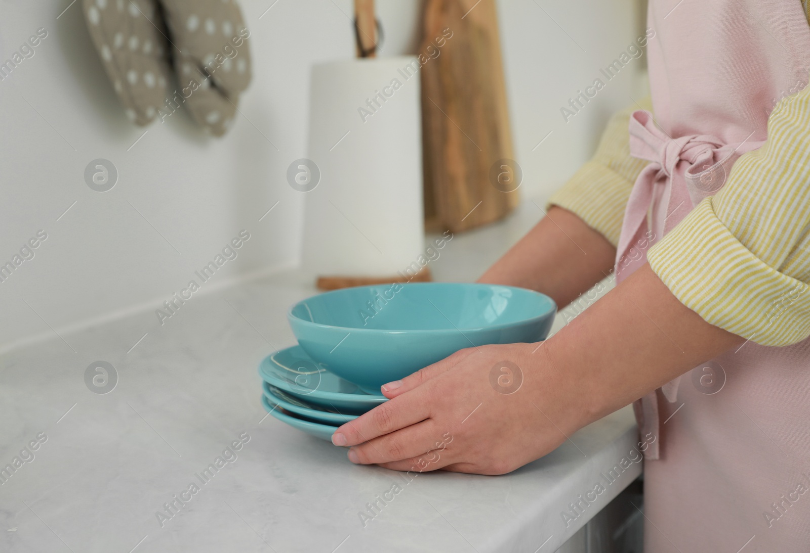 Photo of Woman putting plates on white marble countertop in kitchen, closeup view