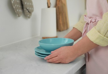 Photo of Woman putting plates on white marble countertop in kitchen, closeup view
