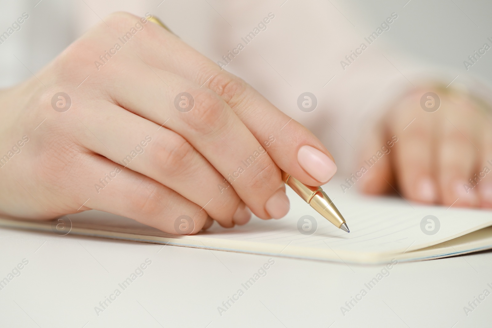 Photo of Woman writing in notebook at white table, closeup