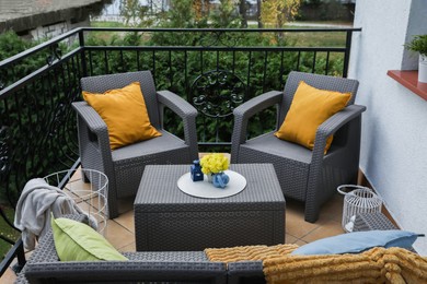 Photo of Colorful pillows, soft blanket and yellow chrysanthemum flowers on rattan garden furniture outdoors