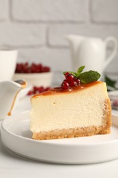 Piece of delicious caramel cheesecake with red currants and mint served on white marble table