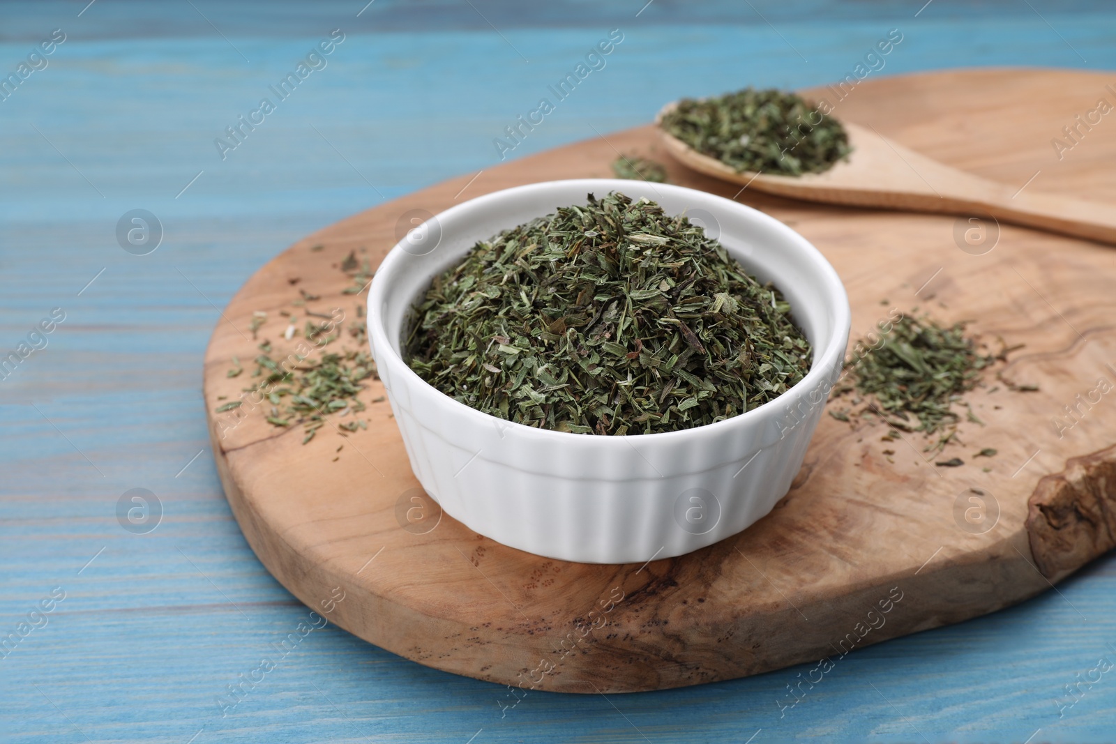 Photo of Bowl with dry tarragon and spoon on light blue wooden table