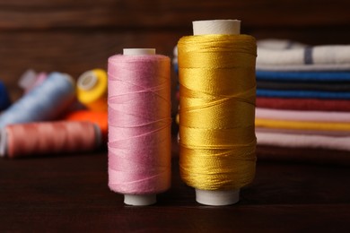 Photo of Different sewing threads on wooden table, closeup. Tailoring accessories