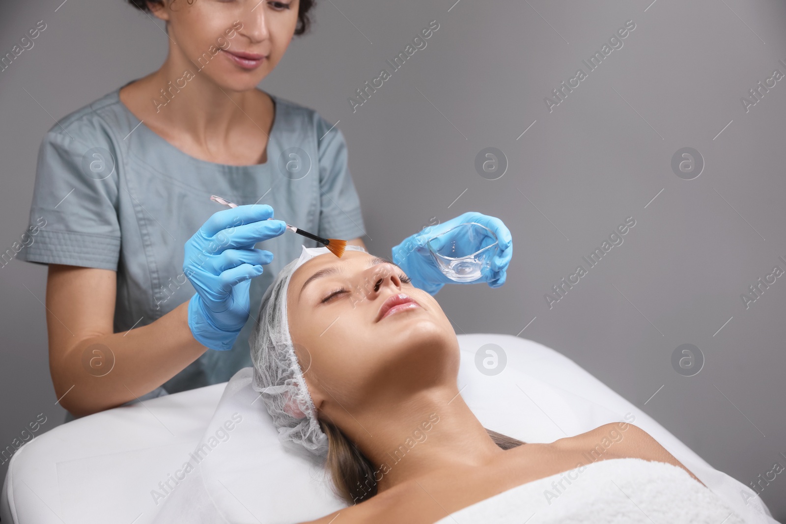 Photo of Cosmetologist applying chemical peel product on client's face in salon