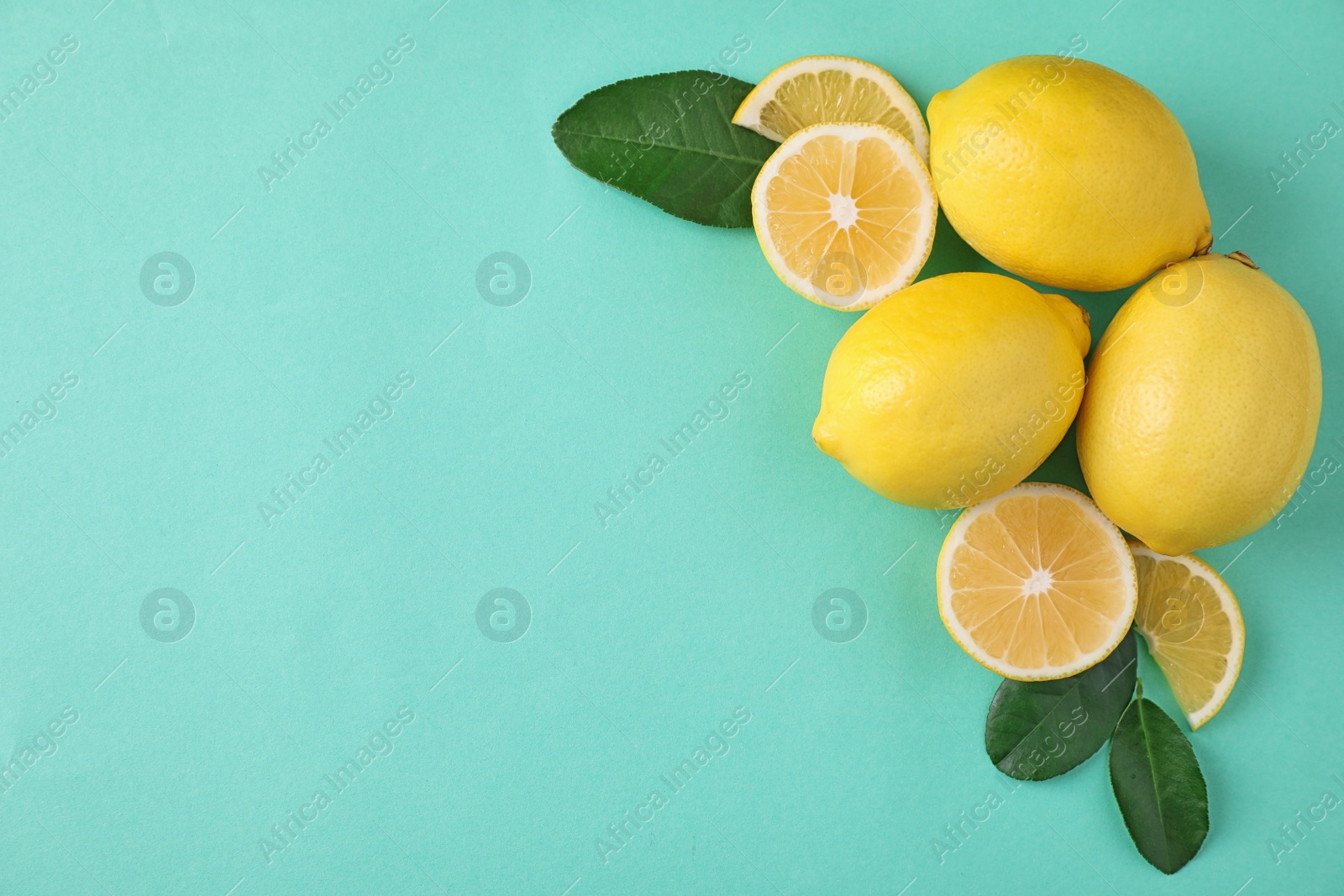 Photo of Fresh lemons and leaves on turquoise background, flat lay. Space for text