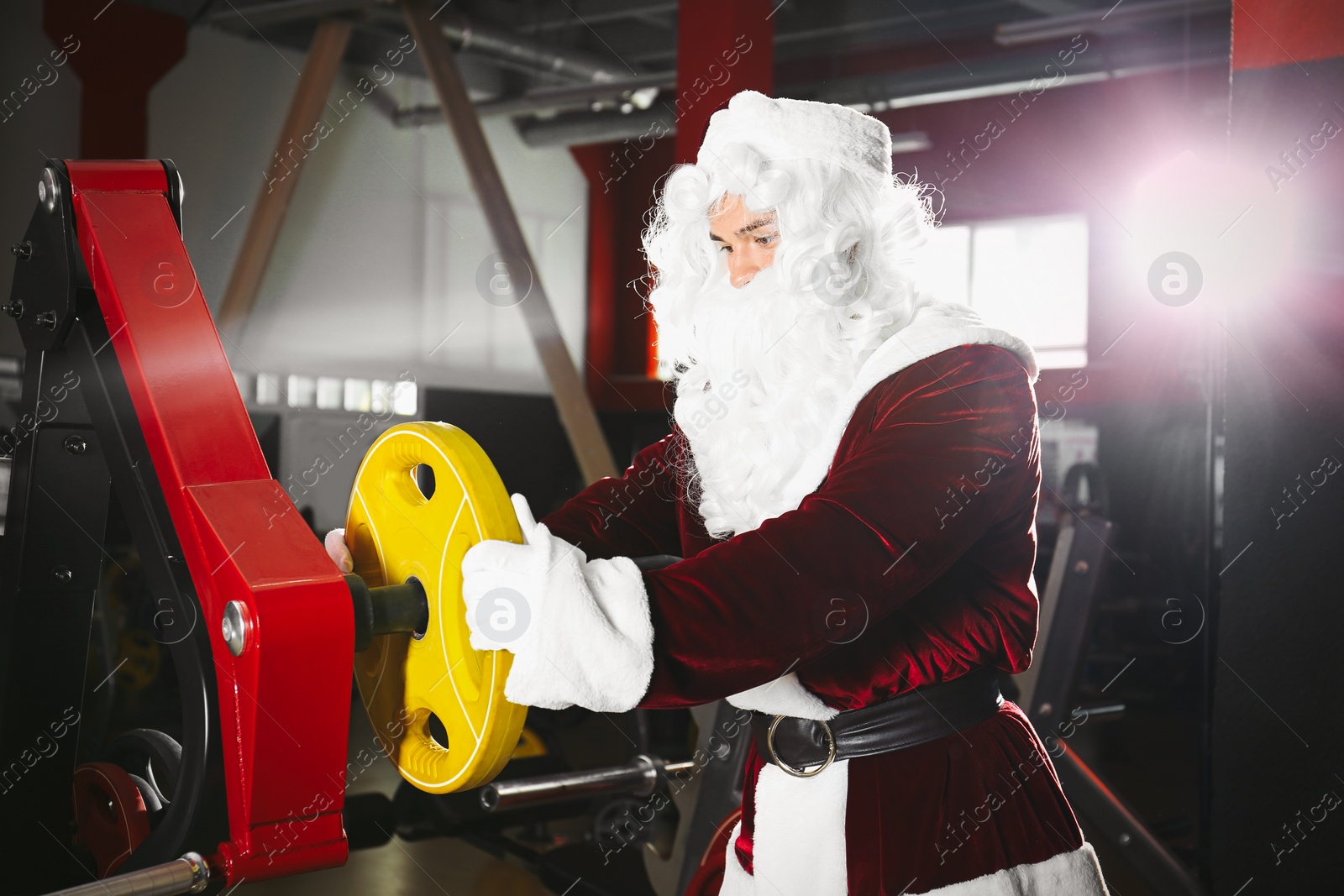 Photo of Young Santa Claus with weight plate in modern gym
