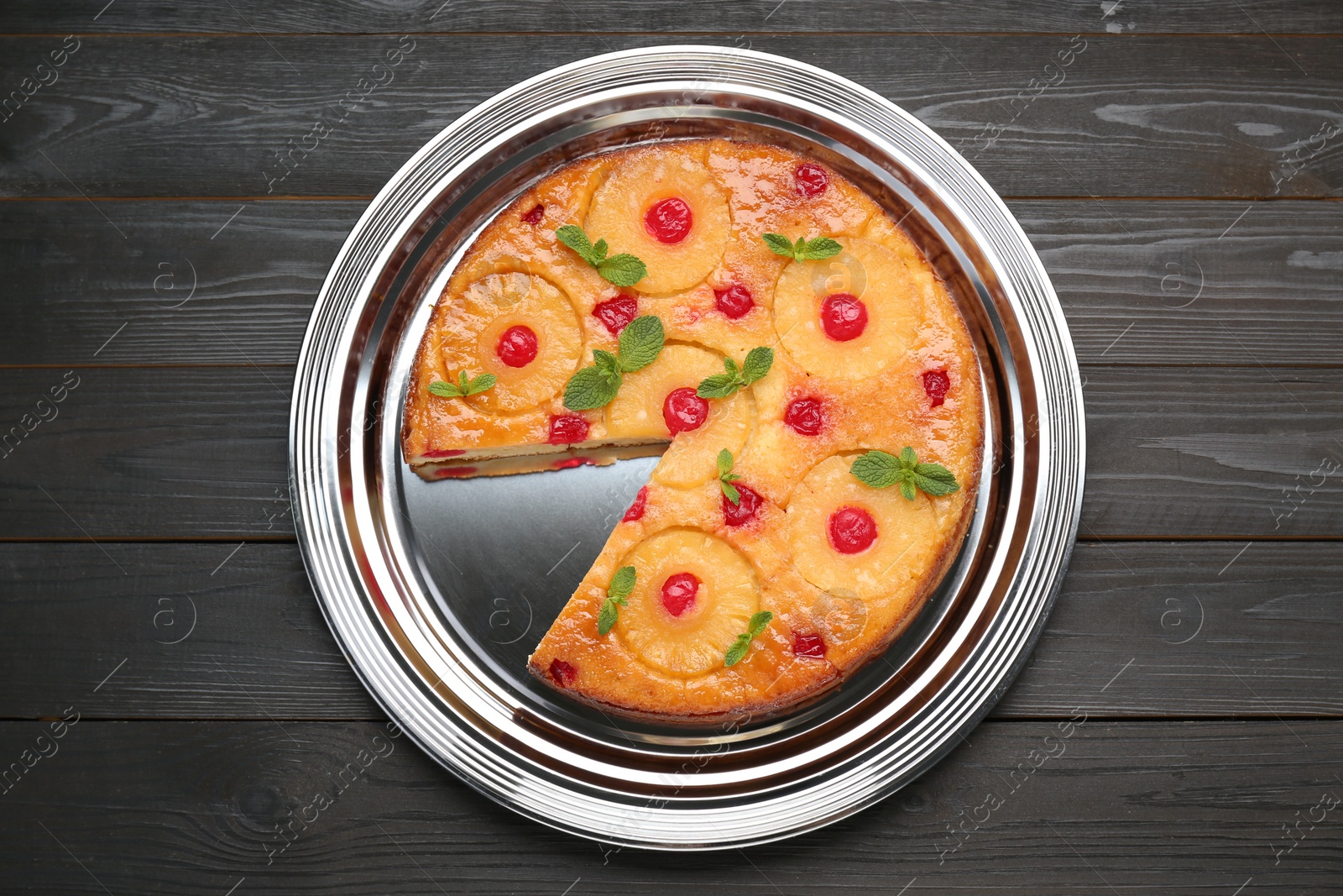 Photo of Delicious cut pineapple pie with cherry and mint on black wooden table, top view