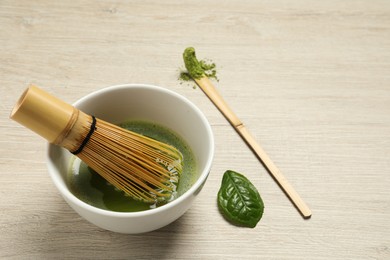 Photo of Cup of fresh green matcha tea with bamboo whisk and spoon on wooden table, space for text
