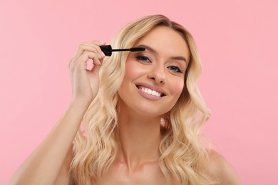 Photo of Beautiful makeup. Smiling woman applying mascara on pink background