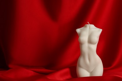 Photo of Beautiful female body shaped candle on red fabric, space for text