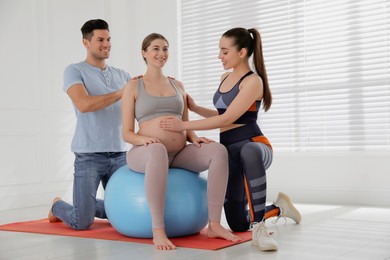 Pregnant woman and her husband working with trainer in gym. Preparation for child birth