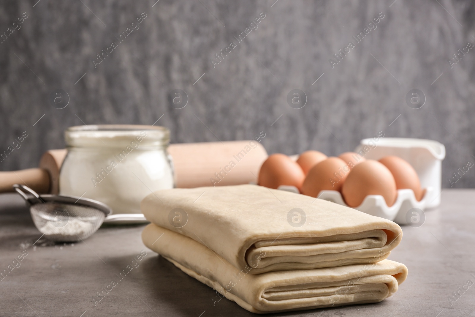 Photo of Composition with fresh dough on table against grey background, space for text. Puff pastry