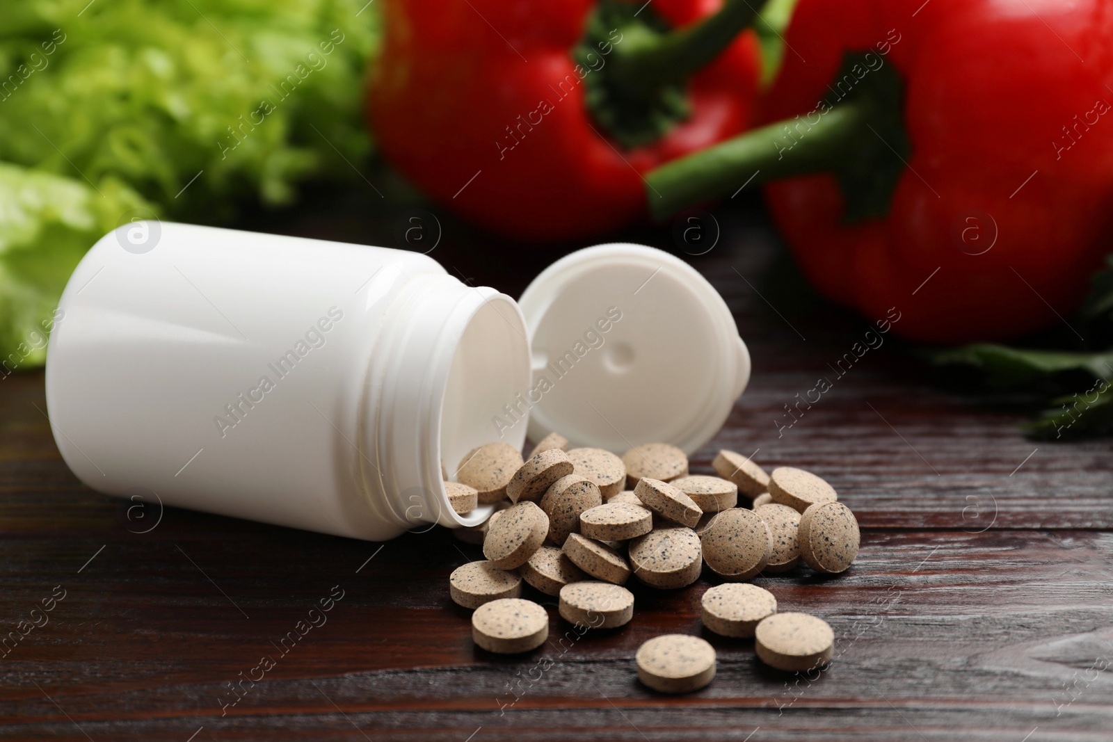 Photo of Dietary supplements. Overturned bottle, pills and food products on wooden table, closeup