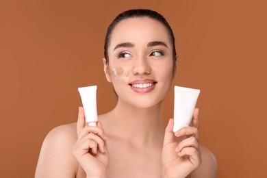 Photo of Woman holding tubes of foundation on brown background