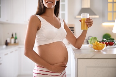Photo of Young pregnant woman with glass of juice in kitchen, closeup. Taking care of baby health