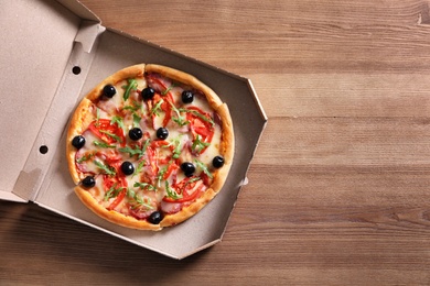 Photo of Cardboard box with tasty pizza on wooden background, top view with space for text