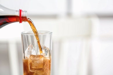 Pouring cola from bottle into glass on blurred background, closeup. Space for text