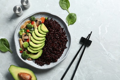 Photo of Plate of boiled brown rice with avocado served on table, top view. Space for text