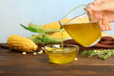 Photo of Woman pouring fresh corn oil into bowl on wooden table