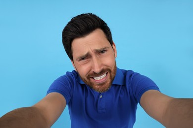 Emotional man taking selfie on light blue background