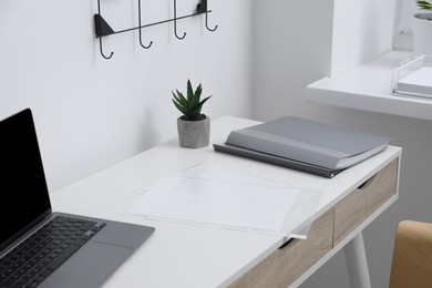 Photo of Punched pockets, folders and laptop on white table in office