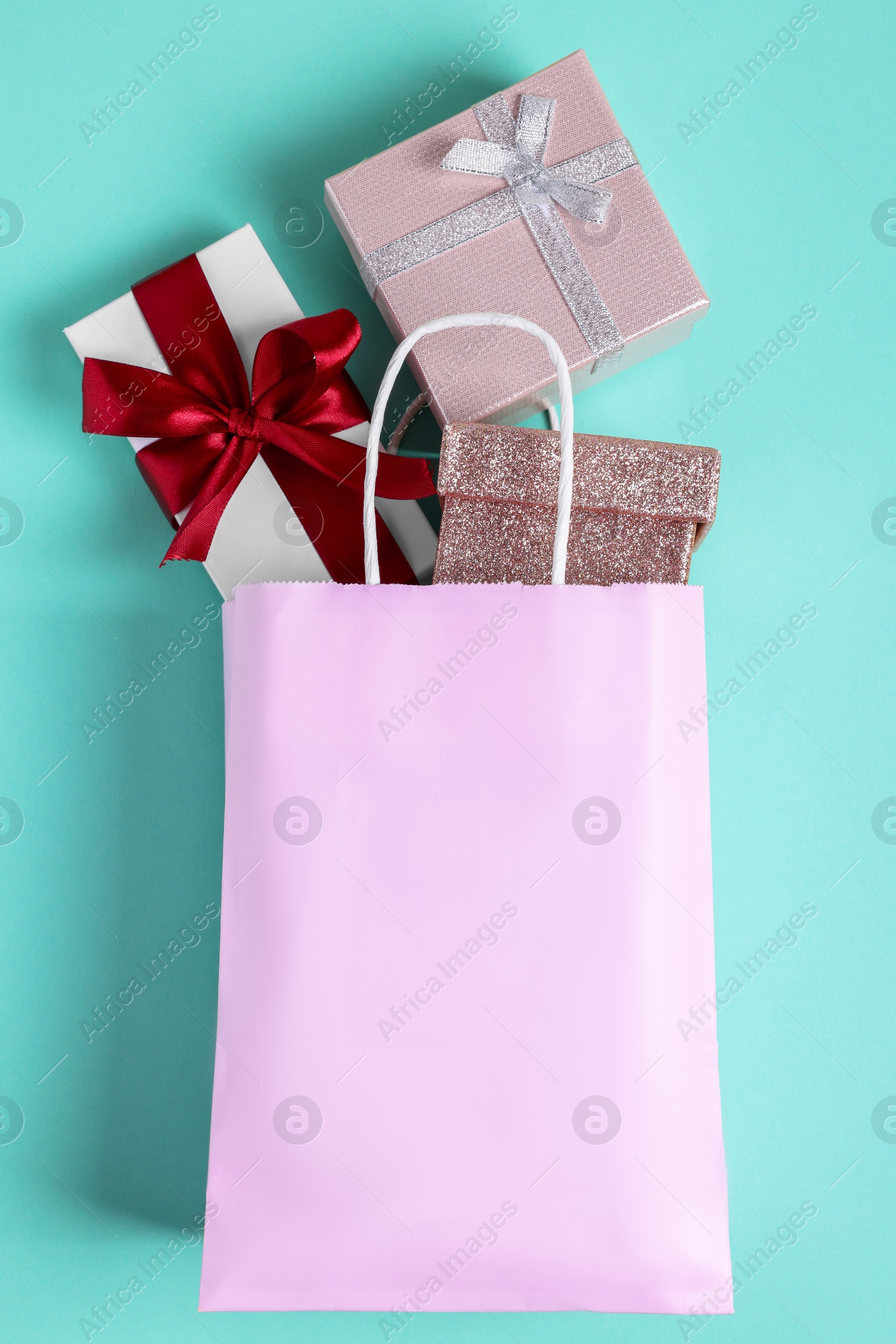 Photo of Pink paper shopping bag full of gift boxes on turquoise background, flat lay