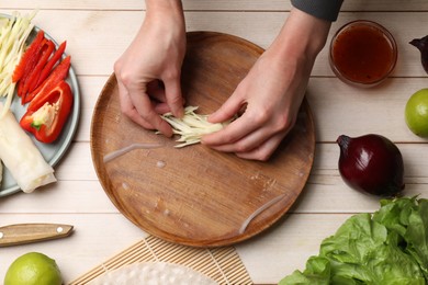 Making delicious spring rolls. Woman wrapping fresh cabbage into rice paper at wooden table, top view