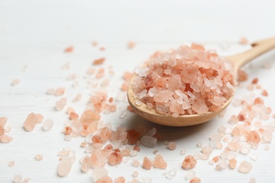 Photo of Spoon and pink himalayan salt on white wooden table, closeup