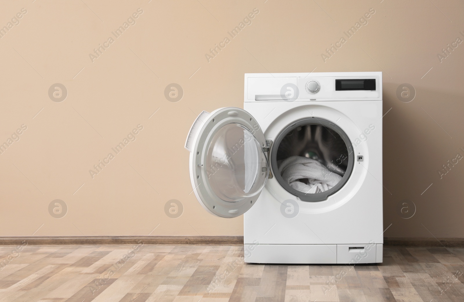 Photo of Modern washing machine with laundry near color wall, space for text