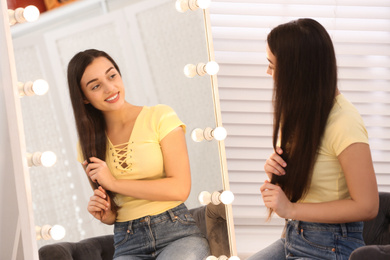 Beautiful young woman looking at herself in large mirror indoors